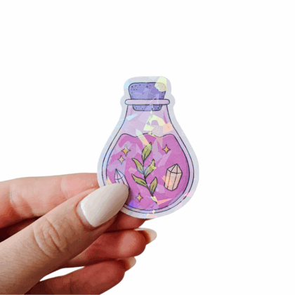 Hand holding a hand-drawn pink-purple potion bottle sticker with green leaves, crystal illustrations, and holographic sparkle overlay. Perfect magical stationery for planners, bullet journals, and gifts.