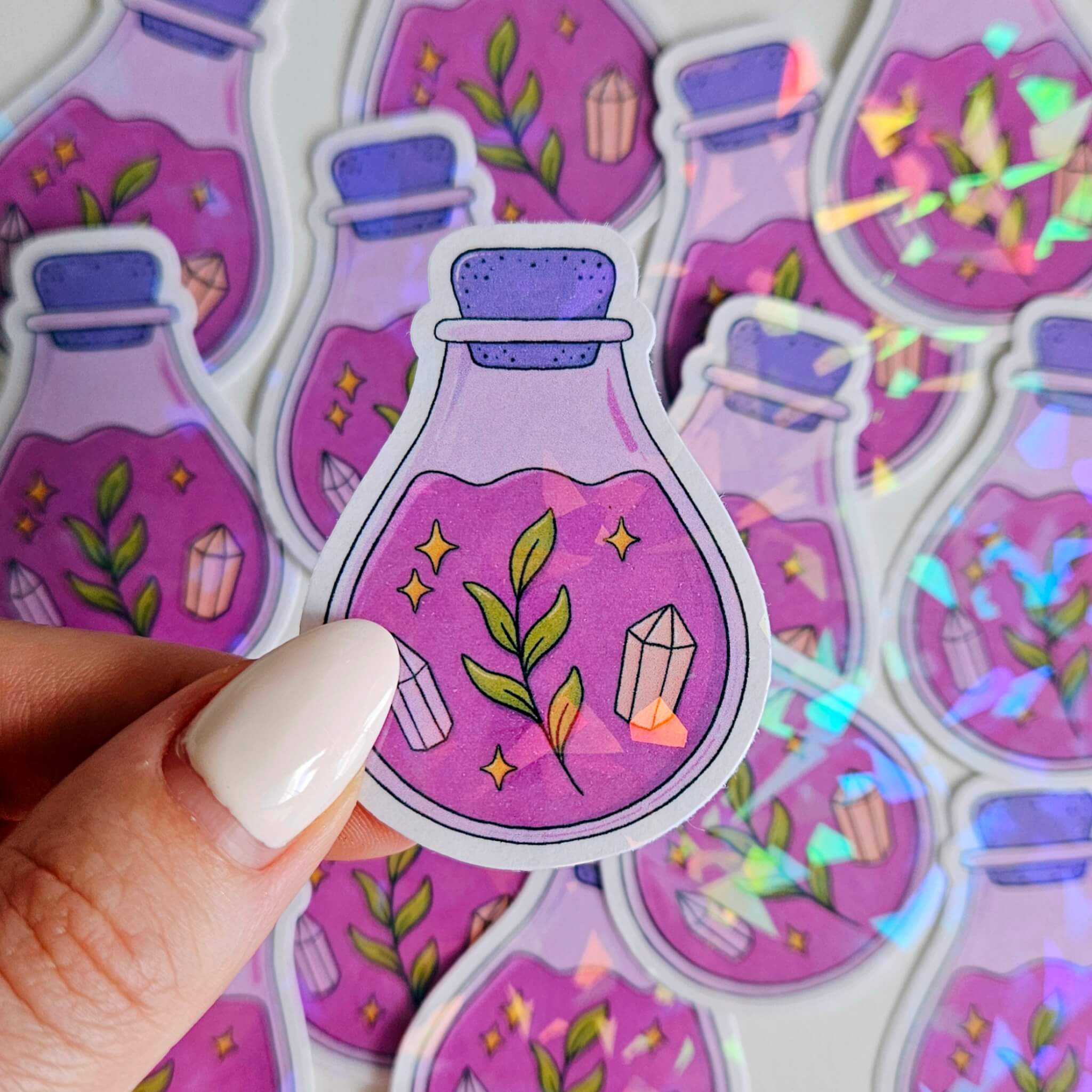 Pink and purple holographic potion bottle sticker with green leaves and crystals, magical cottagecore vinyl decal for journaling and decor.