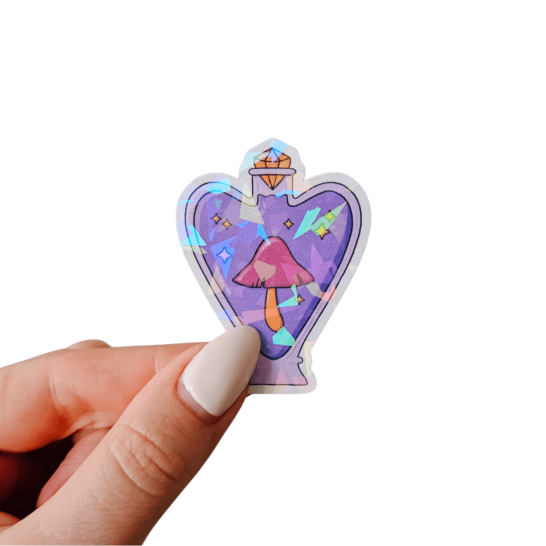 Hand holding a purple potion bottle sticker in a heart-shaped design with a whimsical pink mushroom inside, holographic star and prism foil. Fantasy-inspired sticker for crafts, scrapbooking, and laptop decor.