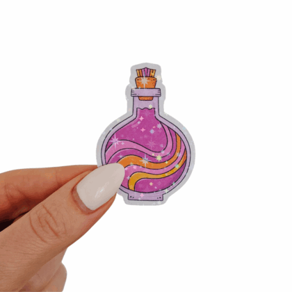 Hand holding a round potion bottle sticker with pink, purple, and orange swirling liquid design, topped with a cork stopper and holographic foil. Hand-drawn magical stationery for planners and creative projects.